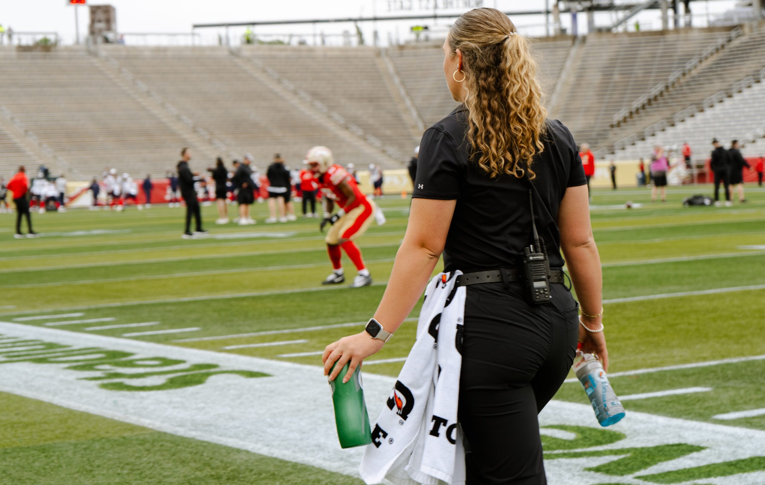 Female trainer walks toward football athletes on the playing field