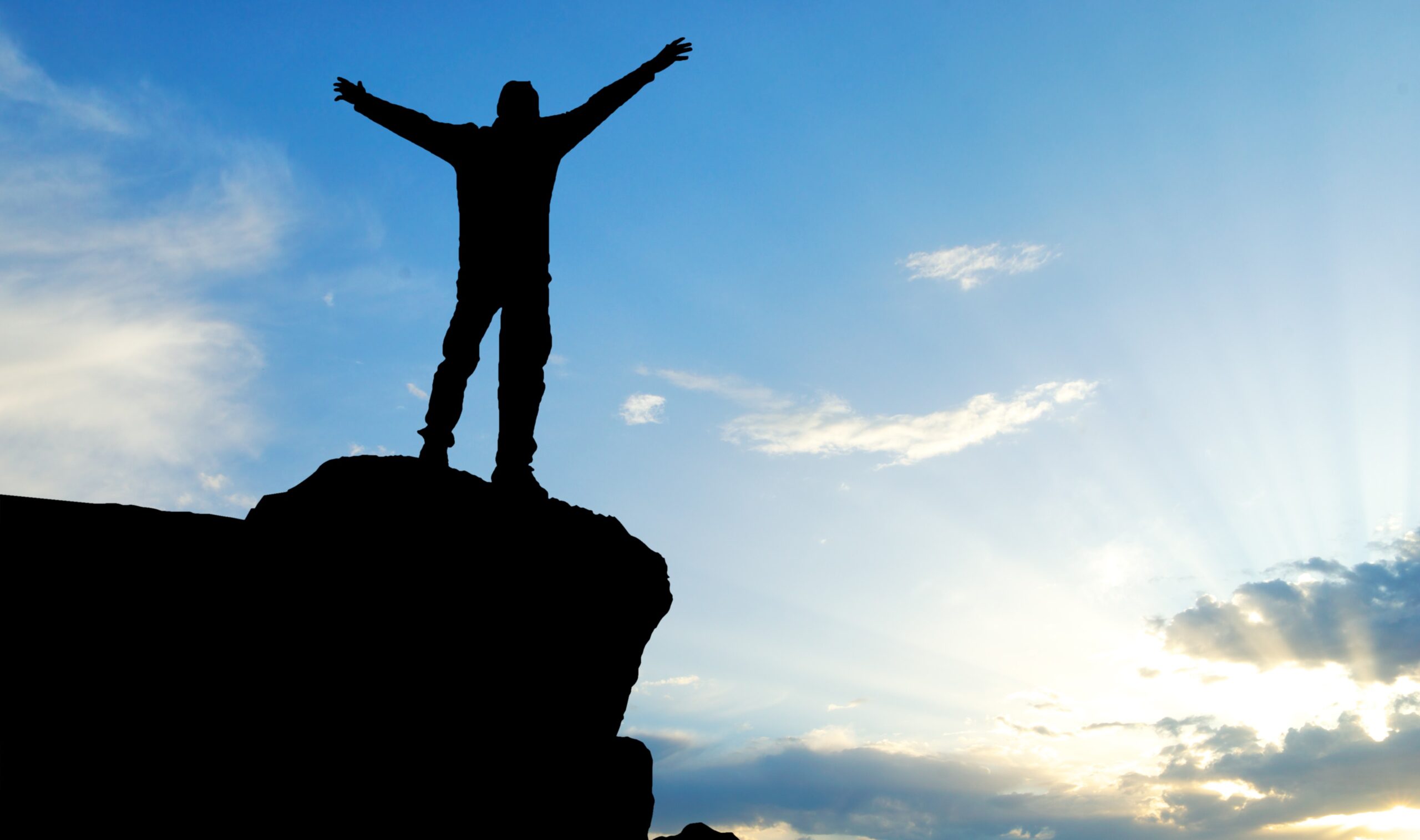 Silhouette of triumphant athlete on rock overlook with sunrise