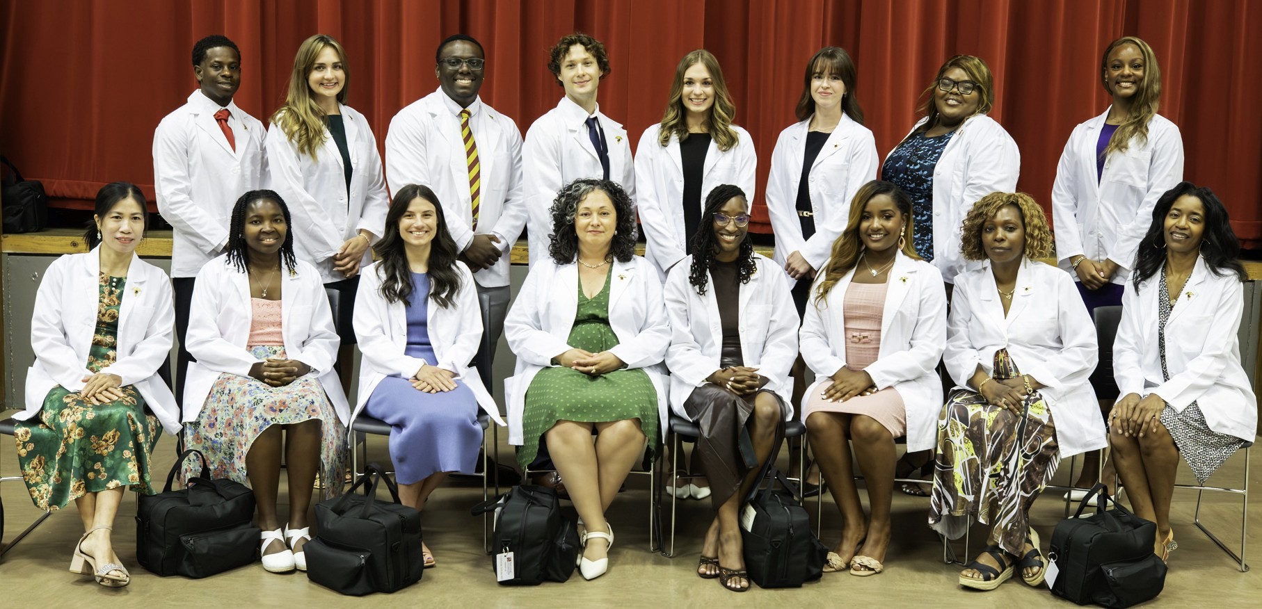 A group of alumni from the National University of Health Sciences pose in white coats.